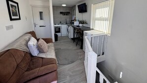 Um espaço compacto com um sofá marrom, uma área de cozinha com micro-ondas e uma televisão fixada na parede.