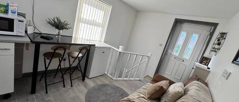 A compact living space with a kitchenette, a dining area, a sofa, and a door leading to an outdoor area.