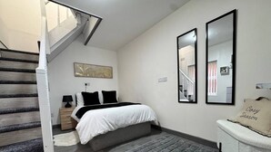 Quarto com cama, mesa de cabeceira, luminária, tapete, espelho e escada.