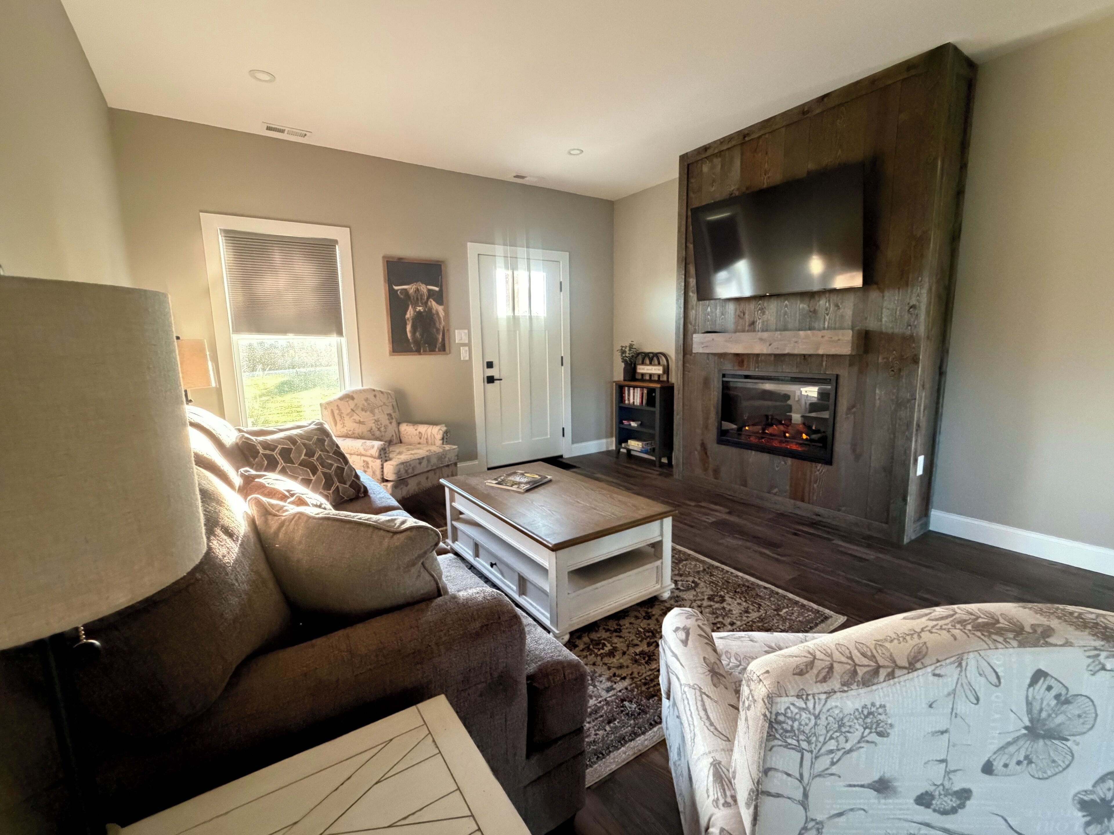 Een woonkamer met een bank, fauteuil, salontafel, open haard en een televisie bevestigd aan een houten wand.