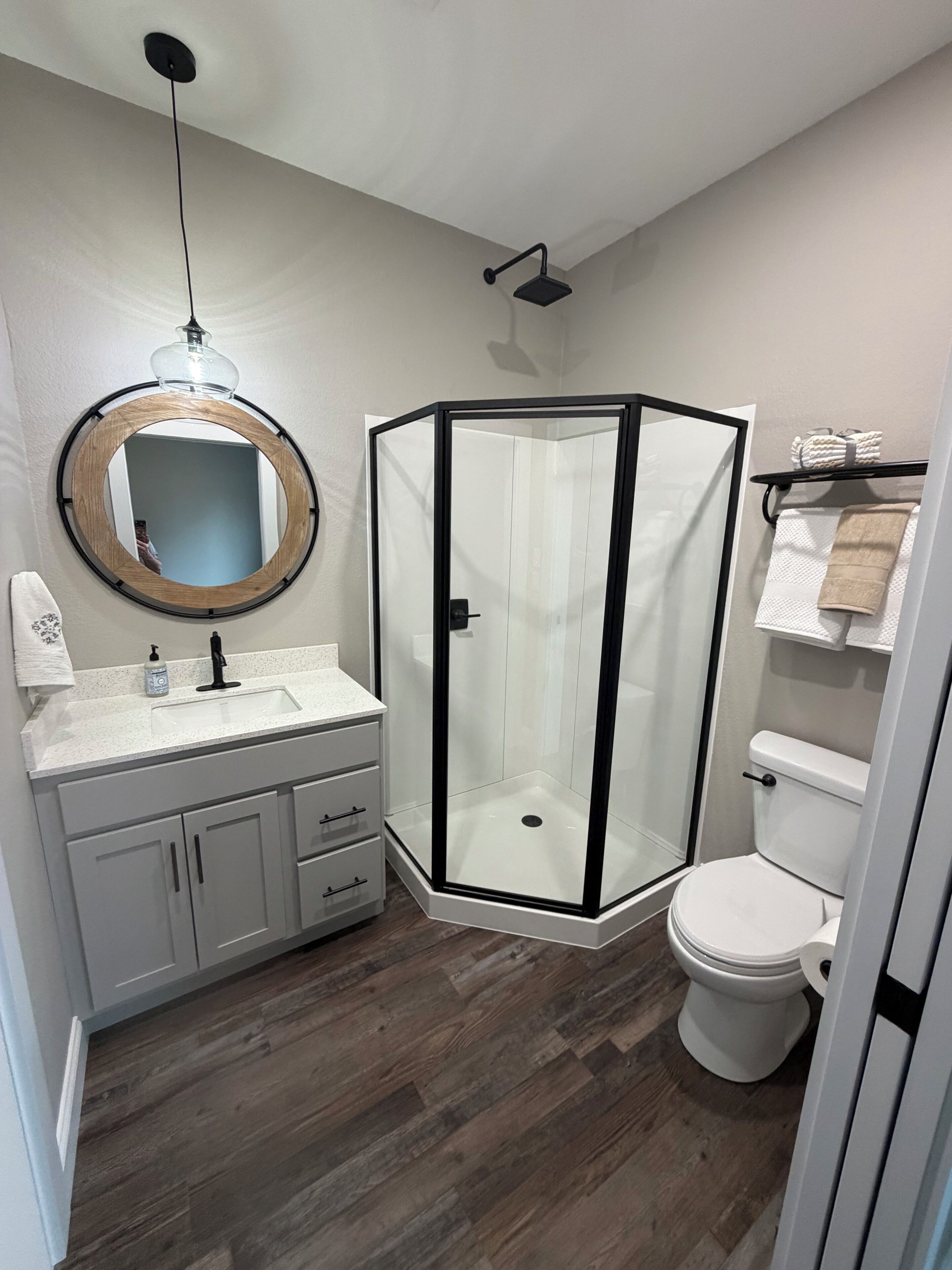 A modern bathroom with a glass shower enclosure, a round mirror, a white sink, and a toilet.