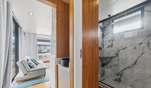 A modern bathroom with a shower, a marble wall, and a view of the outdoors.