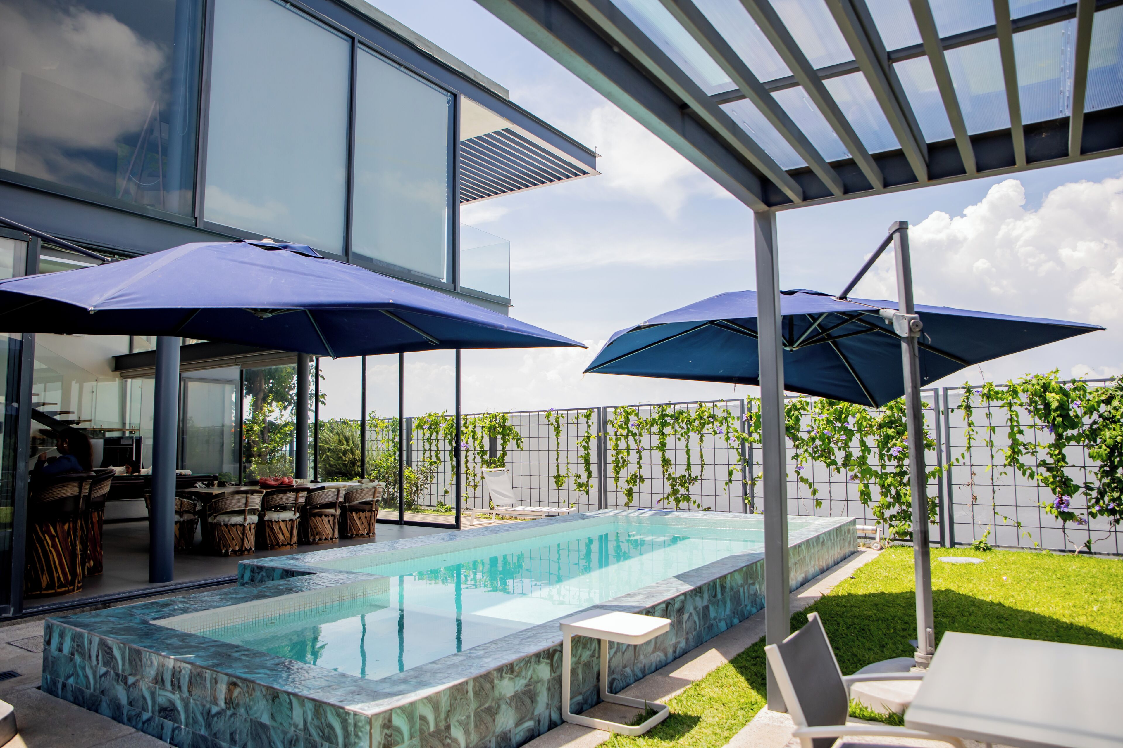 A modern outdoor pool area with a glass enclosure, lounge chairs, and umbrellas.