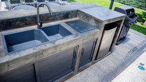 Een buitenkeuken met twee spoelbakken, een kraan en een barbecue.