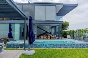 Ein modernes Haus mit Glasfassade, Swimmingpool und überdachter Terrasse.