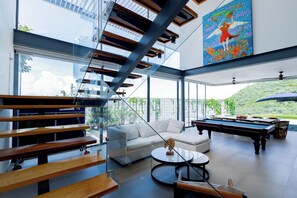 A modern interior with a pool table, a sofa, and a staircase.
