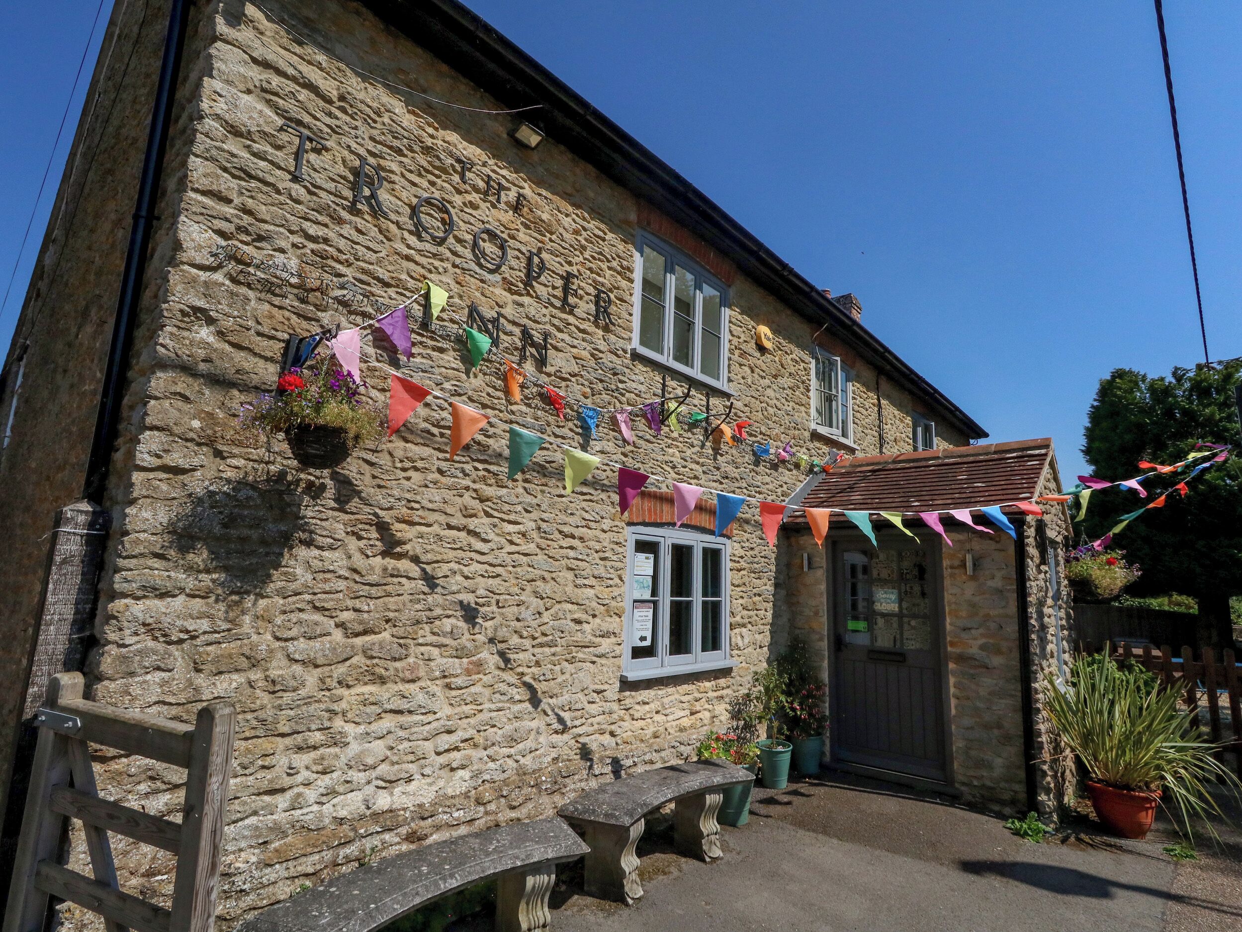 A stone building with a sign reading 'The Rope.' It has a small porch with a bench and potted plants.