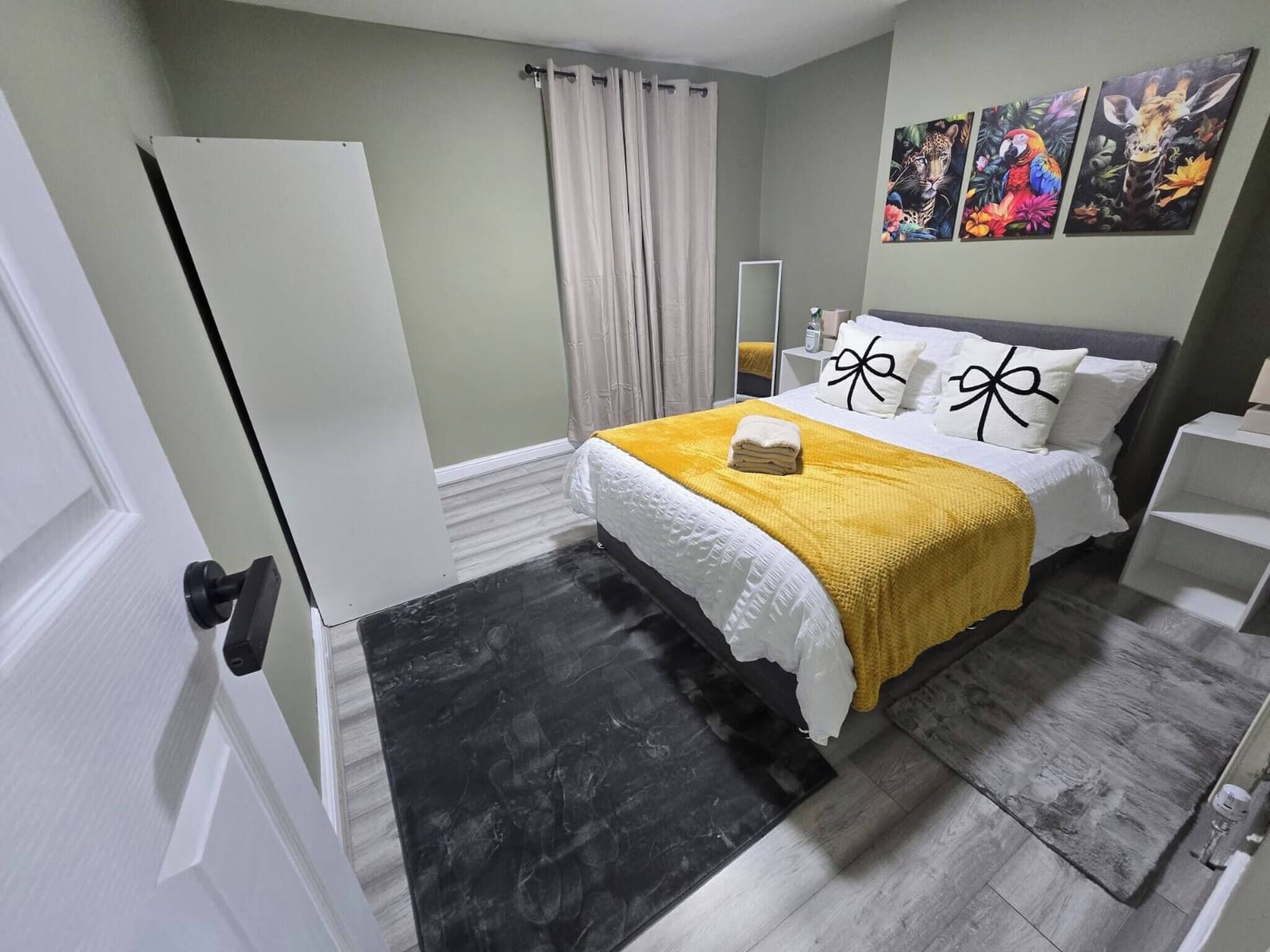 A bedroom with a bed, a bedside table, a mirror, and artwork on the wall.