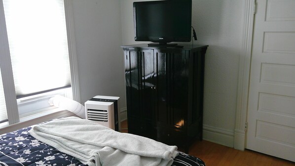 A bedroom with a bed, a television on a stand, a heater, and a door.
