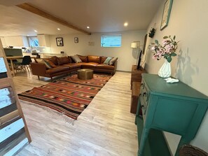 A living room with a brown leather sectional sofa, a patterned rug, a teal side table, and a white vase with flowers.