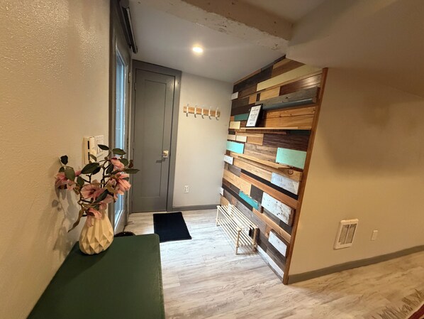 A hallway with a wooden wall panel, a bench, a door, and a plant.