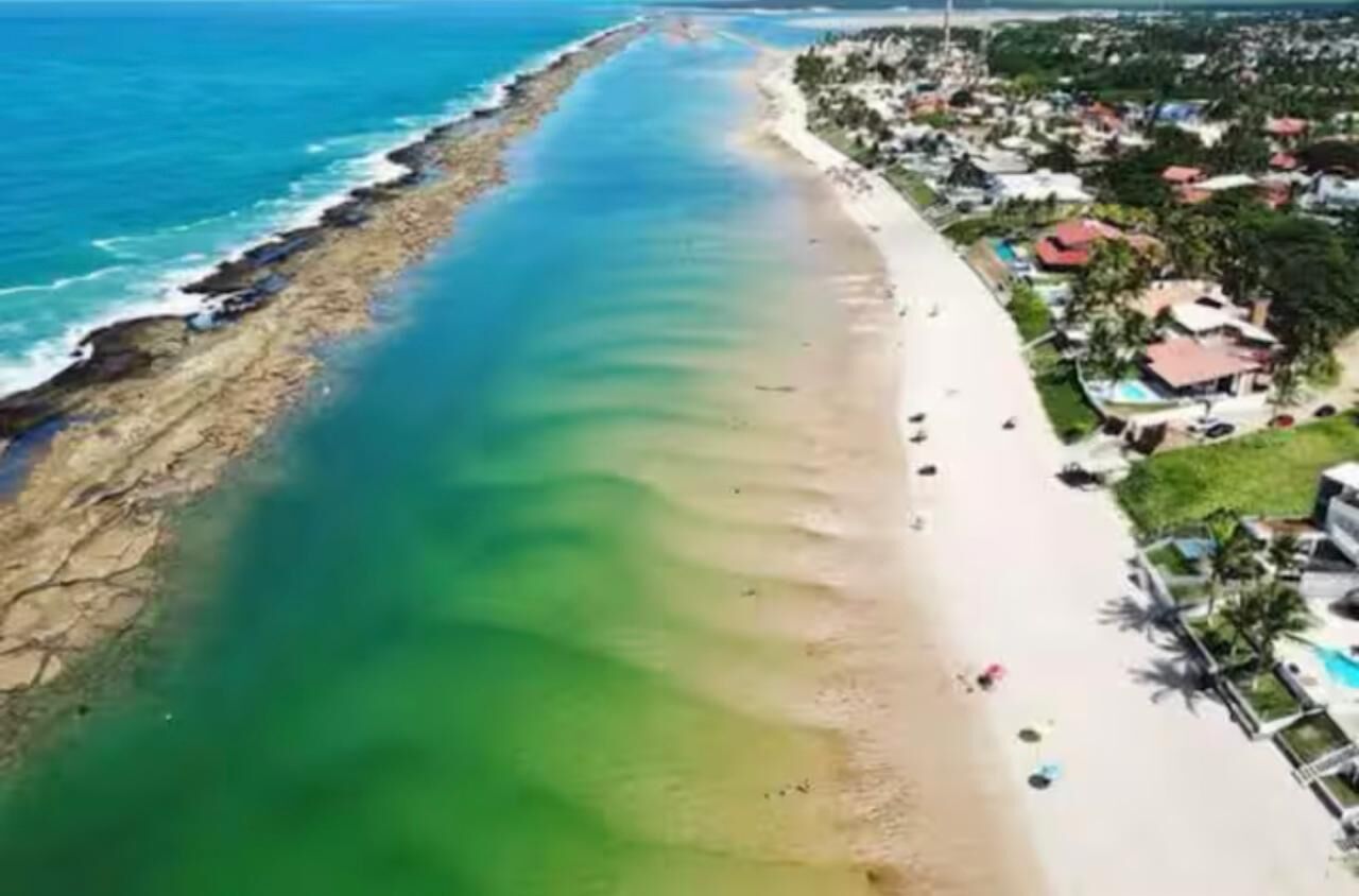 Vista aérea de uma área costeira com praia, casas e mar azul cristalino.