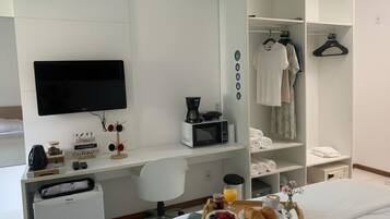 Habitación de hotel con cama, escritorio con televisor, microondas, refrigerador pequeño y cafetera, además de una bandeja para el desayuno.