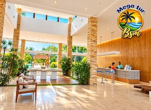 Vestíbulo de hotel con mostrador de recepción, zona de estar y vistas a la piscina.