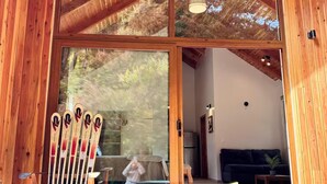 Uma cabana de madeira com uma grande porta de vidro, um suporte para esquis na parte externa e um banco no interior.