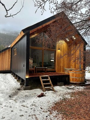 Une cabane aux murs en bois, dotée de grandes fenêtres, d’un porche et d’un escalier en bois menant à l’entrée.