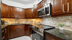 A kitchen with dark wooden cabinets, a stainless steel microwave, a built-in oven, and a granite countertop. - Ocean View Large Condo in Beachfront Resort 1108 (Miami)