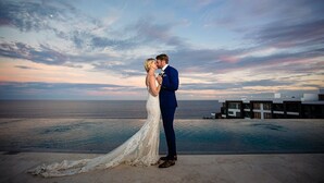 A couple embracing by a pool with a view of the ocean and modern buildings in the background. - 4,198ft² Oceanfront Presidential Suite · Jacuzzi Terrace · Butler · Sleeps 8 (B.C.S.)