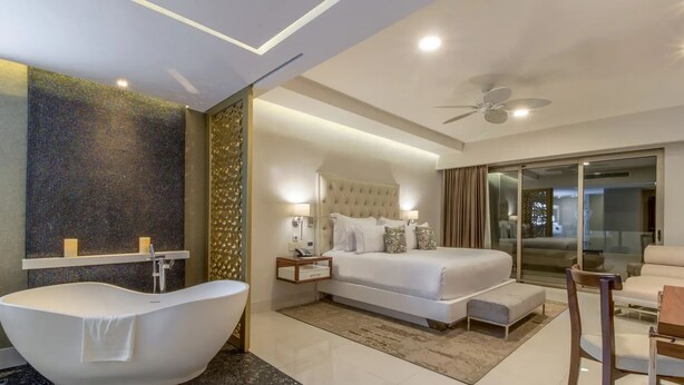 A modern hotel room with a large bed, a bathtub, a ceiling fan, and a glass door leading to a balcony. - 4,198ft² Oceanfront Presidential Suite · Jacuzzi Terrace · Butler · Sleeps 8 (B.C.S.)
