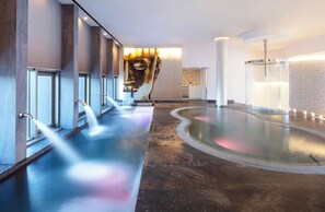 Ein Wellnessbereich mit großem beheiztem Pool, mehreren Brausen und einer Wandskulptur.