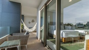 A modern hotel room with a glass door, a hammock, a bed, and a seating area with a chair and a small table. - 4,198ft² Oceanfront Presidential Suite · Jacuzzi Terrace · Butler · Sleeps 8 (B.C.S.)