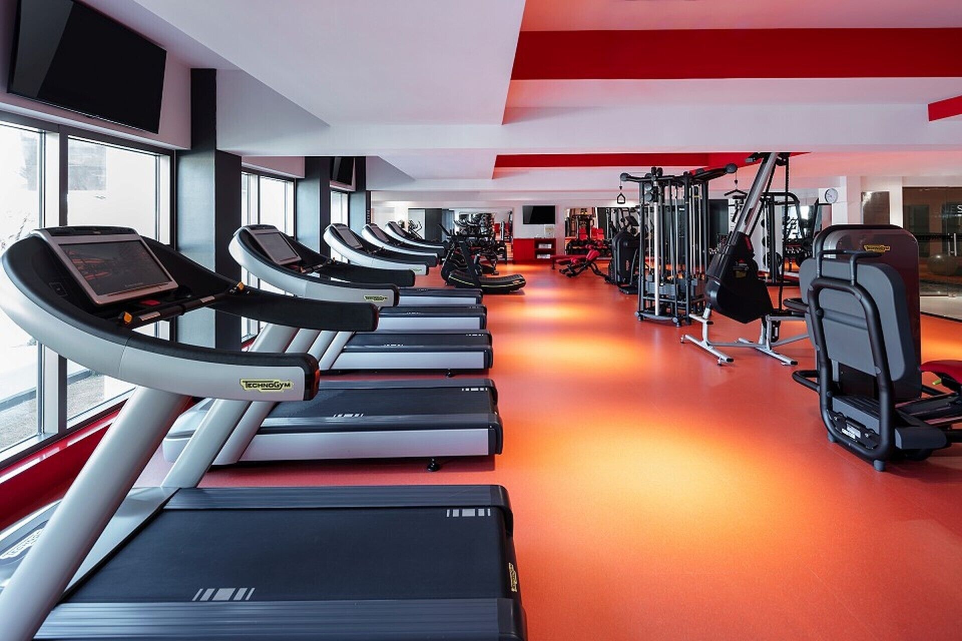 A gym with multiple treadmills, weight machines, and a red-orange floor.