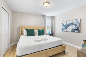 Habitació d'hotel amb un llit gran, un capçal, un quadre a la paret i una finestra amb cortines.