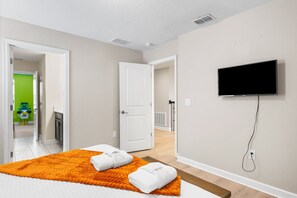 A modern hotel room with a bed, a TV, and a bathroom visible through an open door. - Themed 9BR Villa, Pool, Game Room, Champions Gate (Davenport)