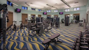 Ein Fitnessstudio mit verschiedenen Trainingsgeräten, mehreren Fernsehbildschirmen und einem gemusterten Teppich.