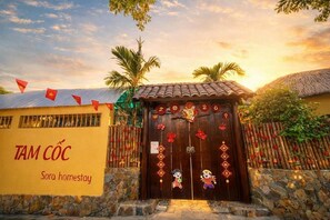 Een traditionele Vietnamese gastenverblijf met een houten deur, versierd met rode en gouden details, een stenen muur en een rieten dak.