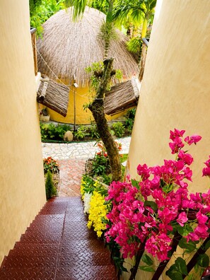 A narrow pathway leading to a thatched-roof structure, surrounded by vibrant bougainvillea and a palm tree. - Sora Tam Coc  (Nam Hoa Lu)