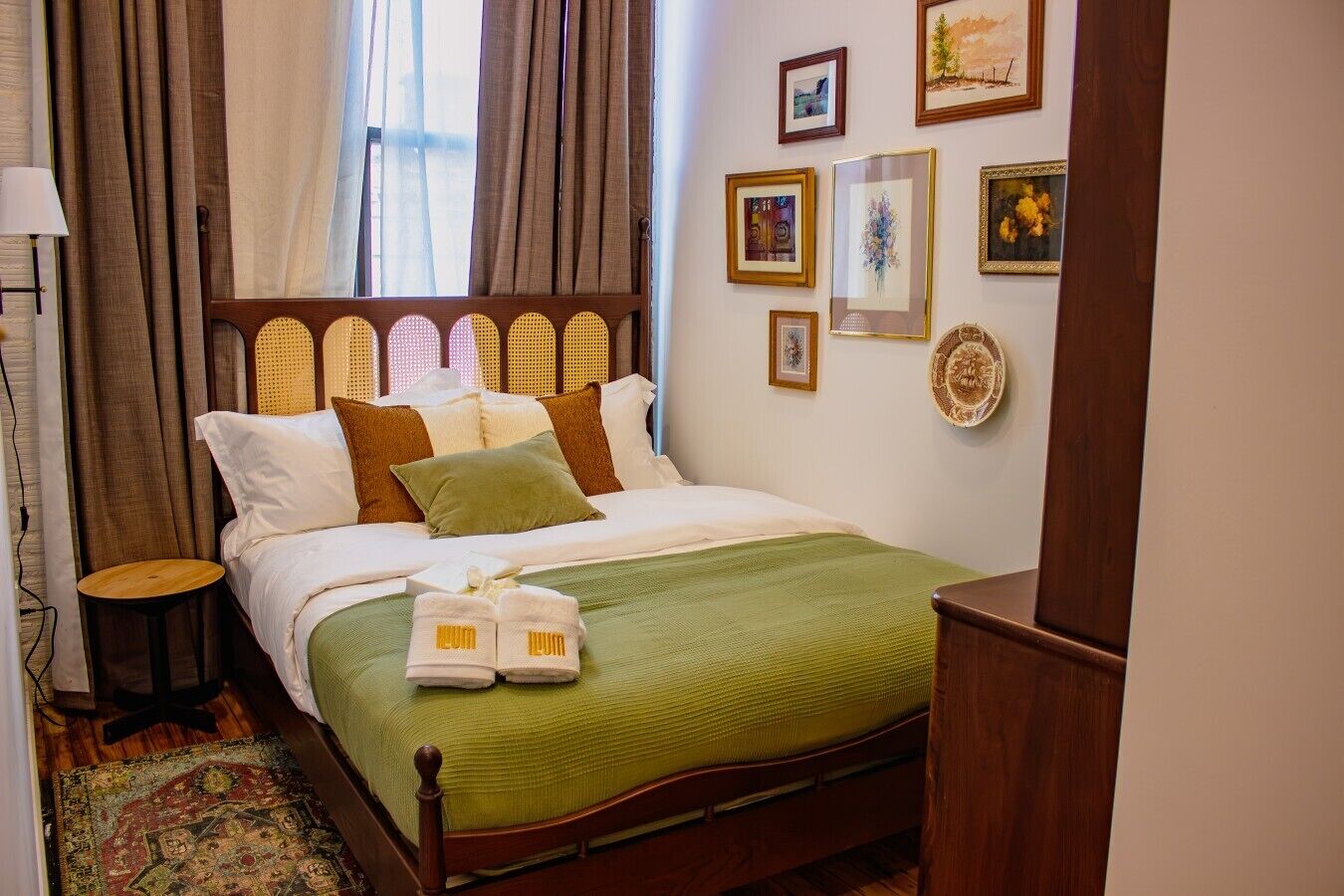 Quarto de hotel com cama, mesa de cabeceira, luminária, janela com cortinas e obra de arte na parede.