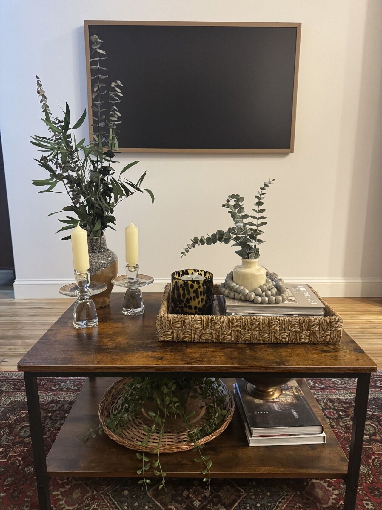 Une table basse en bois, agrémentée d’objets décoratifs, d’un livre et d’un tableau encadré, posée sur un tapis à motifs.