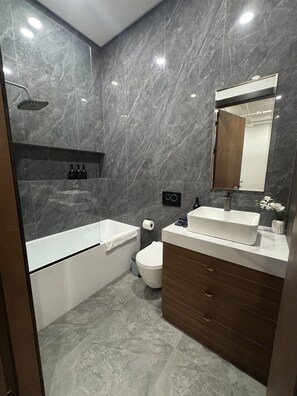 Et moderne badeværelse med badekar, toilet og et vaskeskab med spejl.