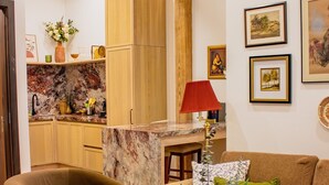 Ein Wohnzimmer mit einer Couch, einem Couchtisch mit Dekoration, einer roten Lampe und einer Küchenzeile mit Holzschränken und einer Marmorarbeitsplatte.