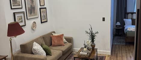 Una sala de estar con un sofá, una mesa de centro, una lámpara de pie y cuadros en la pared.