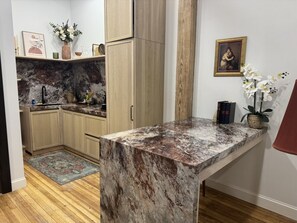 A kitchen with a marble countertop, wooden cabinets, a rug, and decorative items.