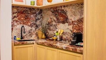 A kitchen with a marble backsplash, wooden cabinets, a sink, and a coffee machine.