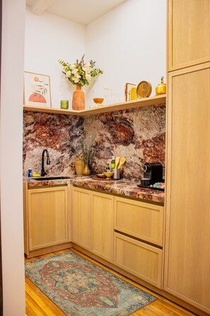 A kitchen with a marble backsplash, wooden cabinets, a sink, and a coffee machine.