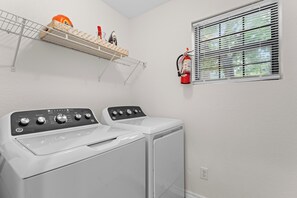 A laundry area with two front-loading washing machines, a shelf with laundry supplies, and a fire extinguisher mounted on the wall. - Sagewood: Two Kings, Fireplace and Pool (Branson)