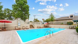 Une piscine entourée d’une clôture et d’arbres, avec des chaises longues et des parasols à proximité.