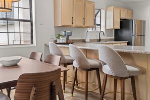 A modern kitchen with a central island, bar stools, a dining table, and a refrigerator. - Sagewood: Two Kings, Fireplace and Pool (Branson)