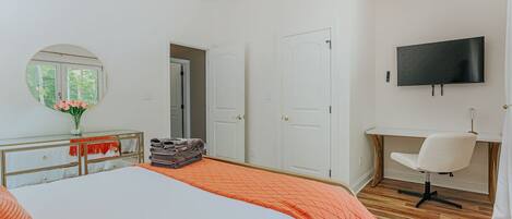 Un dormitorio con cama, escritorio, silla, televisor y espejo.