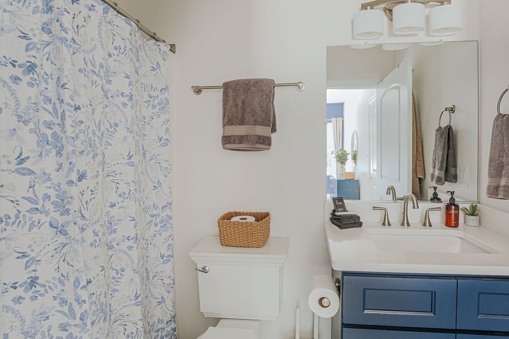 A bathroom with a toilet, a sink with a mirror, a towel rack, and a shower curtain.