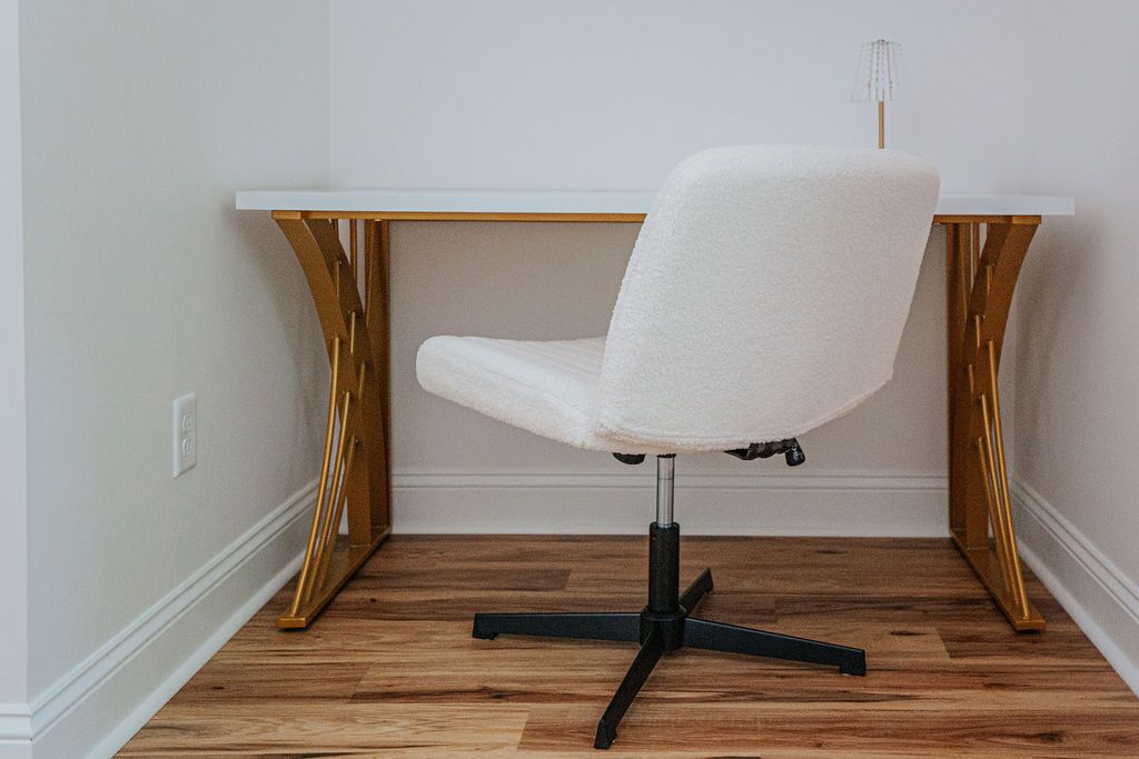 A white office chair with a black base, positioned in front of a white desk with a wooden frame.