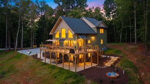 Une maison à deux étages avec une terrasse, entourée d’une forêt.