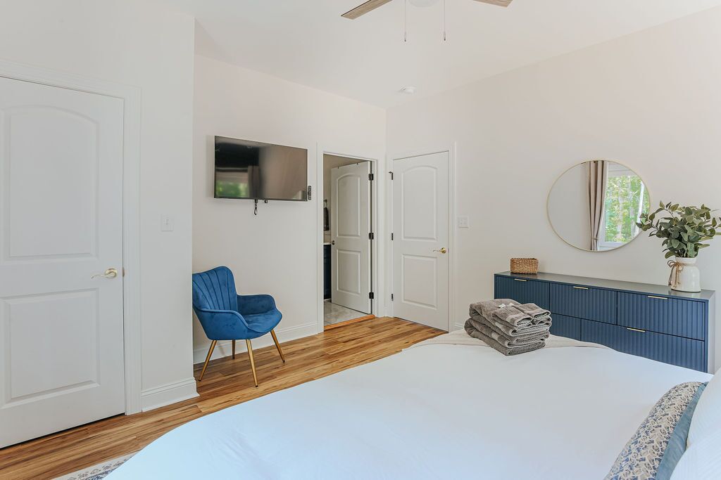 Ein Schlafzimmer mit einem Bett, einem blauen Sessel, einem Schminktisch und einem an der Wand befestigten Fernseher.