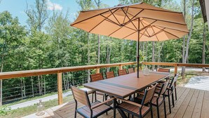 A wooden deck with a table and chairs, an umbrella, and a view of a forest. - On Mountain Time (Roseland)