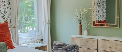 A bedroom with a bed, a dresser, a mirror, and a window with curtains.