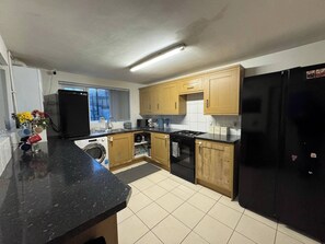 A kitchen with wooden cabinets, a black refrigerator, a washing machine, and a microwave.